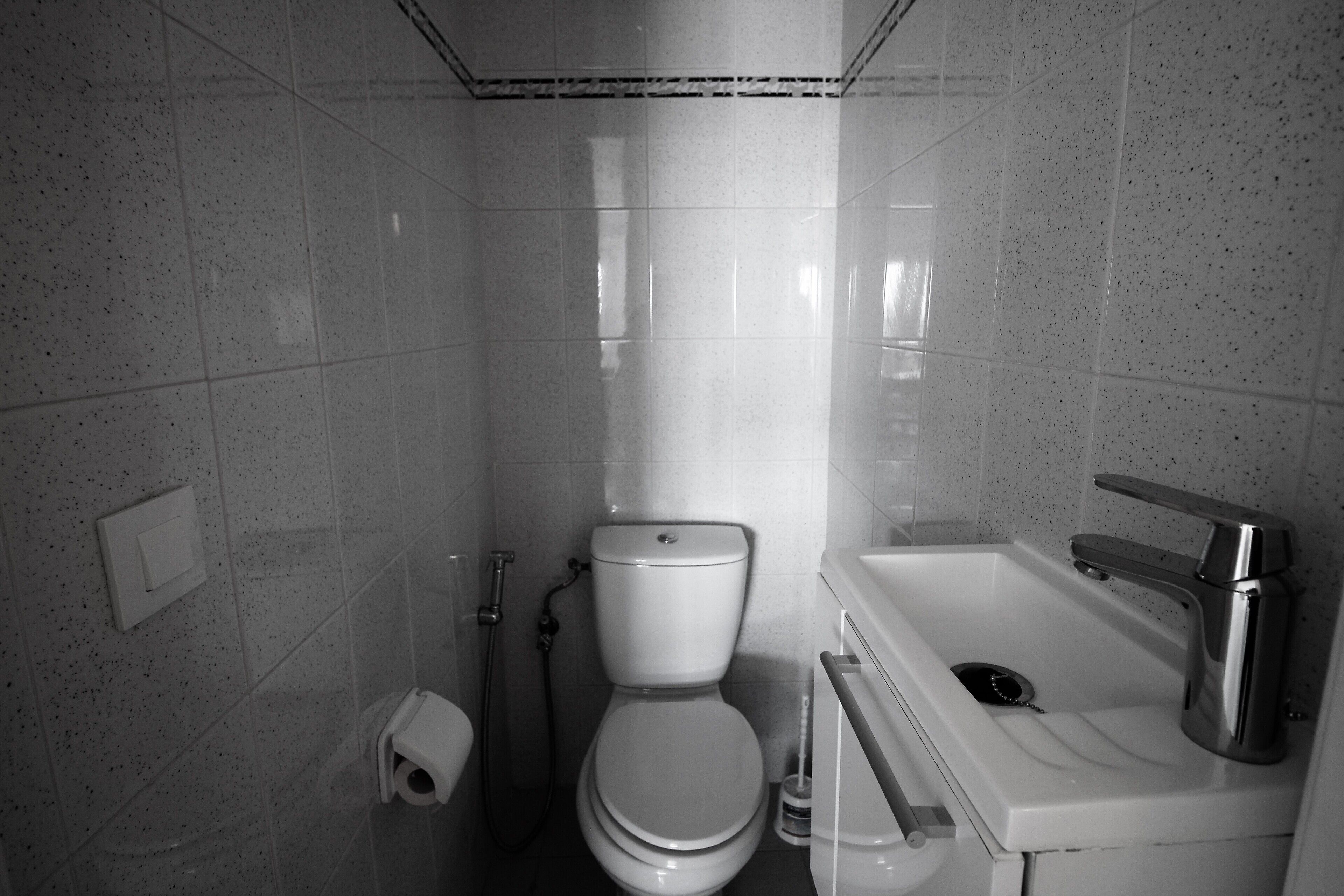 Een kleine betegelde badkamer met toilet, wastafel en douche.