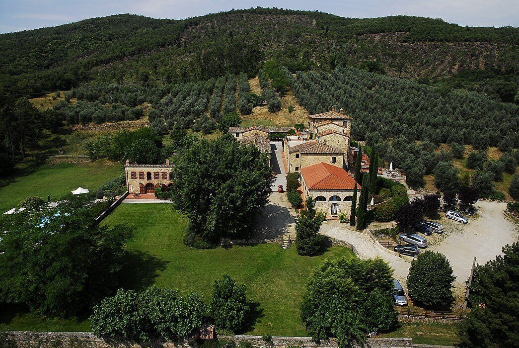 Eine Villa mit rotem Ziegeldach, umgeben von üppiger Vegetation und einer hügeligen Landschaft.