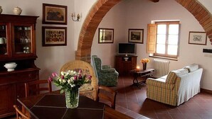 Ein gemütliches Wohnzimmer mit einer Ziegelbogenarchitektur, einem Esstisch mit Stühlen, einer Couch, einem Fernseher und verschiedenen gerahmten Bildern an den Wänden.