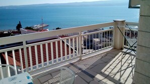 Un balcon avec vue sur la mer, une balustrade blanche et une table avec une chaise.