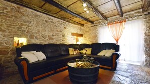 A stone-walled living room with a black leather sofa, a glass coffee table, and a rustic wooden ceiling. - Holiday Home in Vodnjan with Terrace, Air condition, WIFI, Washing machine (3556-1) (Vodnjan)