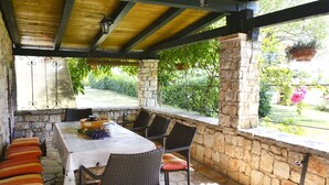 An outdoor patio with a stone wall, a table with chairs, and a view of a garden. - Holiday Home in Vodnjan with Terrace, Air condition, WIFI, Washing machine (3556-1) (Vodnjan)