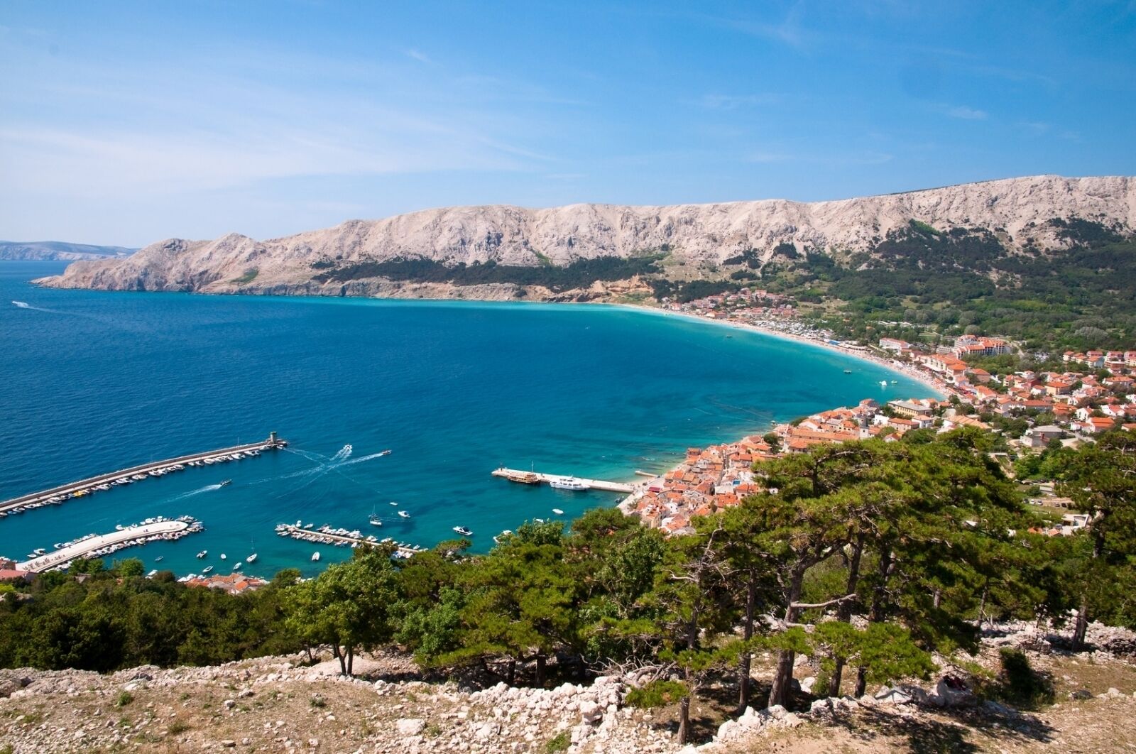 A coastal town with a marina, buildings, and a mountainous backdrop.