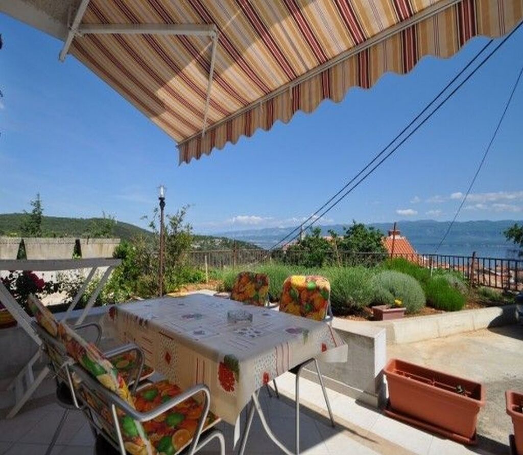 Une terrasse extérieure avec une table et des chaises, un auvent à rayures et une vue sur la mer et les collines.
