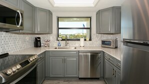 A modern kitchen with grey cabinets, stainless steel appliances, a dishwasher, and a window with a view. - Steps to Siesta Key beach, restaurants and shops! (Sarasota)