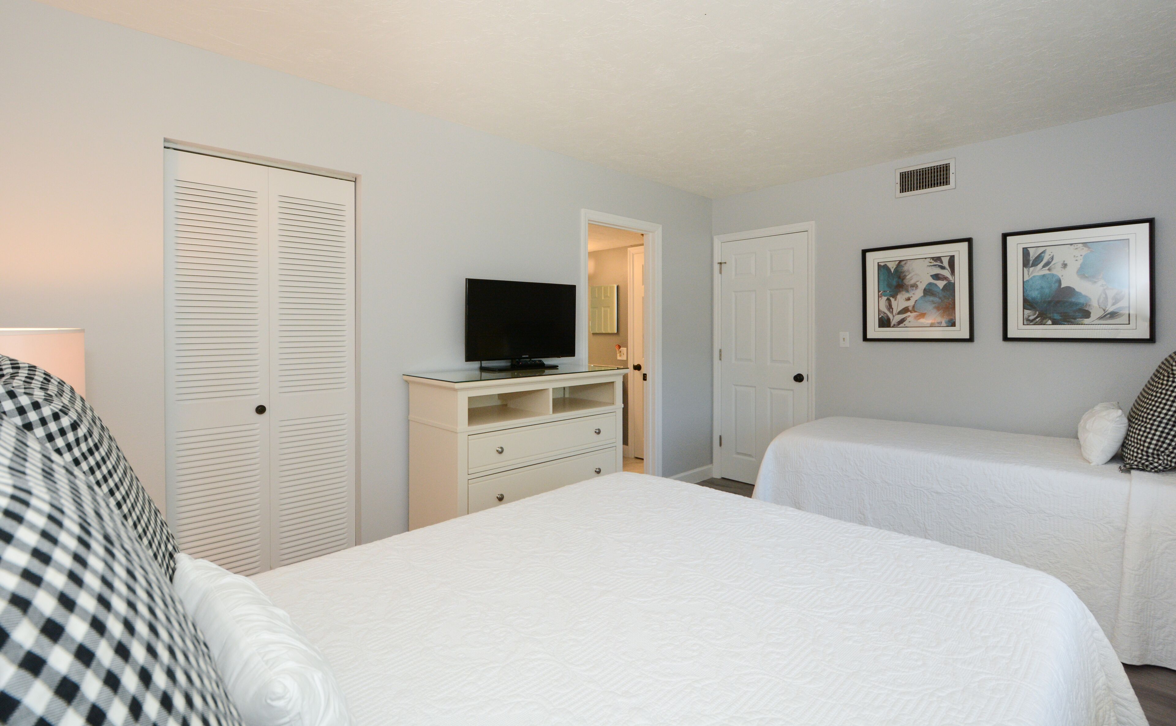 A hotel room with two beds, a TV on a dresser, and two framed pictures on the wall.