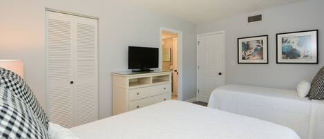 A hotel room with two beds, a TV on a dresser, and two framed pictures on the wall.