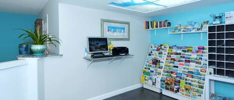 A reception area with a desk, computer, framed picture, potted plant, and a wall display of brochures.