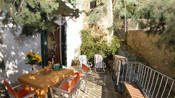 Une terrasse avec une table dressée pour deux personnes, deux chaises à rayures, un vase rempli de fleurs jaunes et une bouteille de bière.