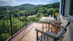 A balcony with a wooden table and chairs, a glass of water, and a vase with flowers.