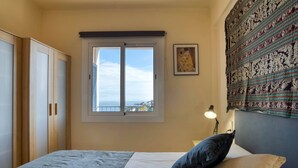 A bedroom with a bed, a window, a lamp, and a tapestry on the wall.