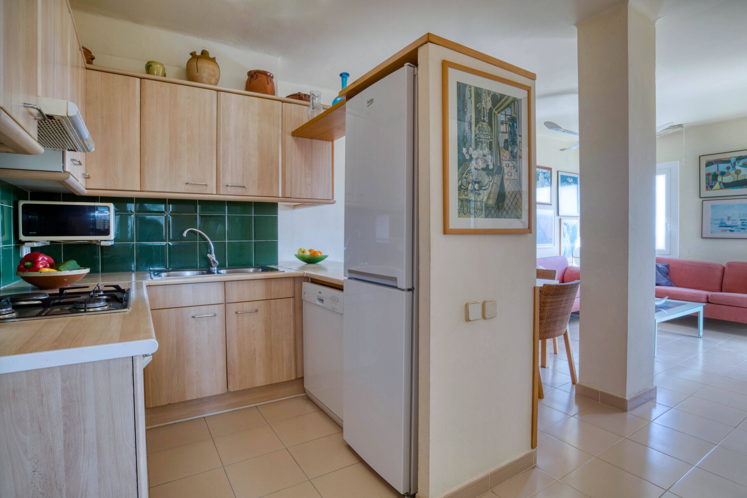 Eine Küche mit Holzausstattung, einer Mikrowelle, einem Kühlschrank und einem Spülbecken. Ein Essbereich mit einem Stuhl und einem Tisch ist ebenfalls vorhanden.