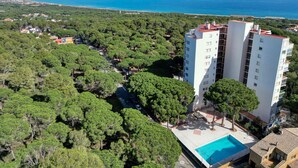 A high-rise building with a rooftop pool, surrounded by dense greenery and a view of the sea.