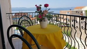 Ein Balkon mit gelbem Tischlein, einem Topf mit Blumen und Blick auf das Meer.