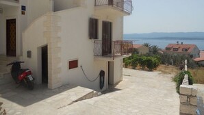 Ein zweistöckiges Gebäude mit Balkon, einem abgestellten Roller und freiem Blick auf das Meer und die entfernten Berge.