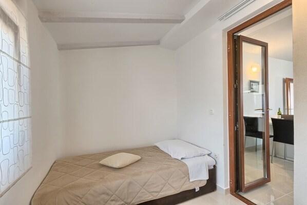 A small, single-bed room with a wooden door leading to a dining area.