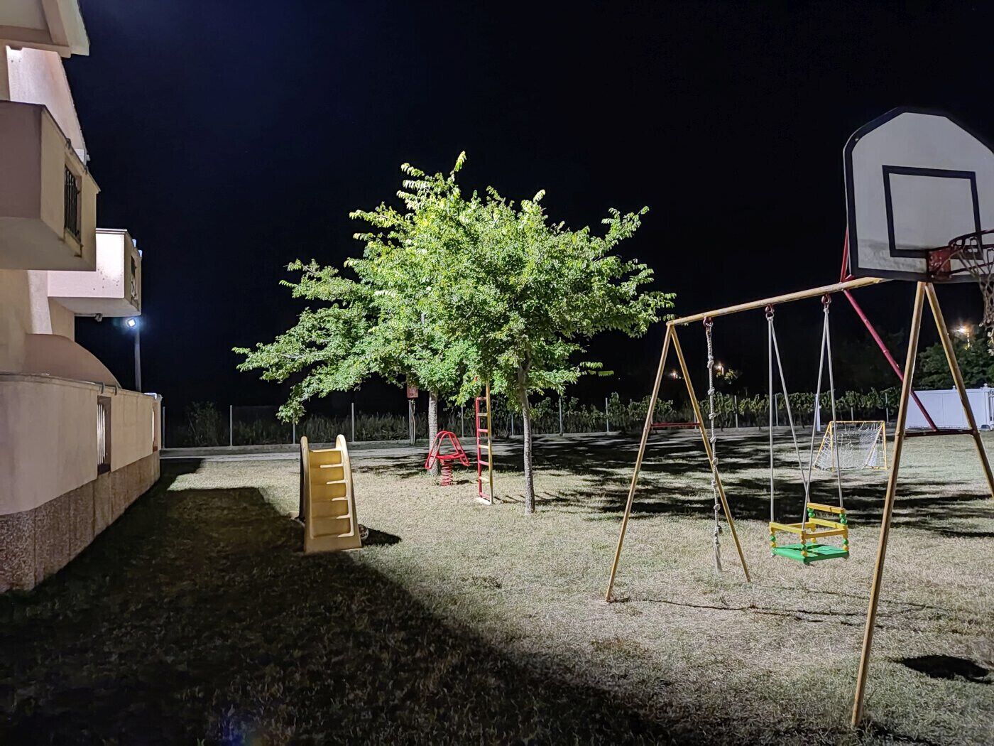 Un parque infantil con columpios y aro de baloncesto de noche.