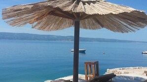 A beachside lounge with a thatched umbrella, wooden lounge chairs, and a view of the sea. - Apartment in Duće with Seaview, Balcony, Air condition, WIFI (237-1) (Duce)