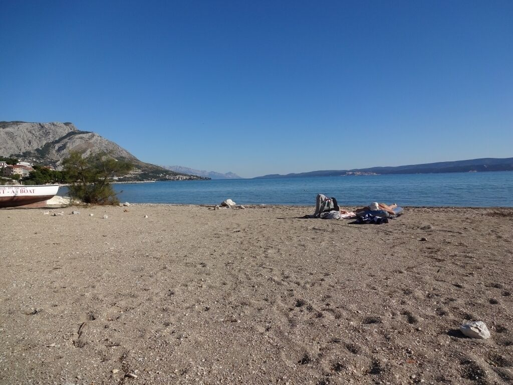 Uma praia com barco, terreno rochoso e montanhas ao longe.