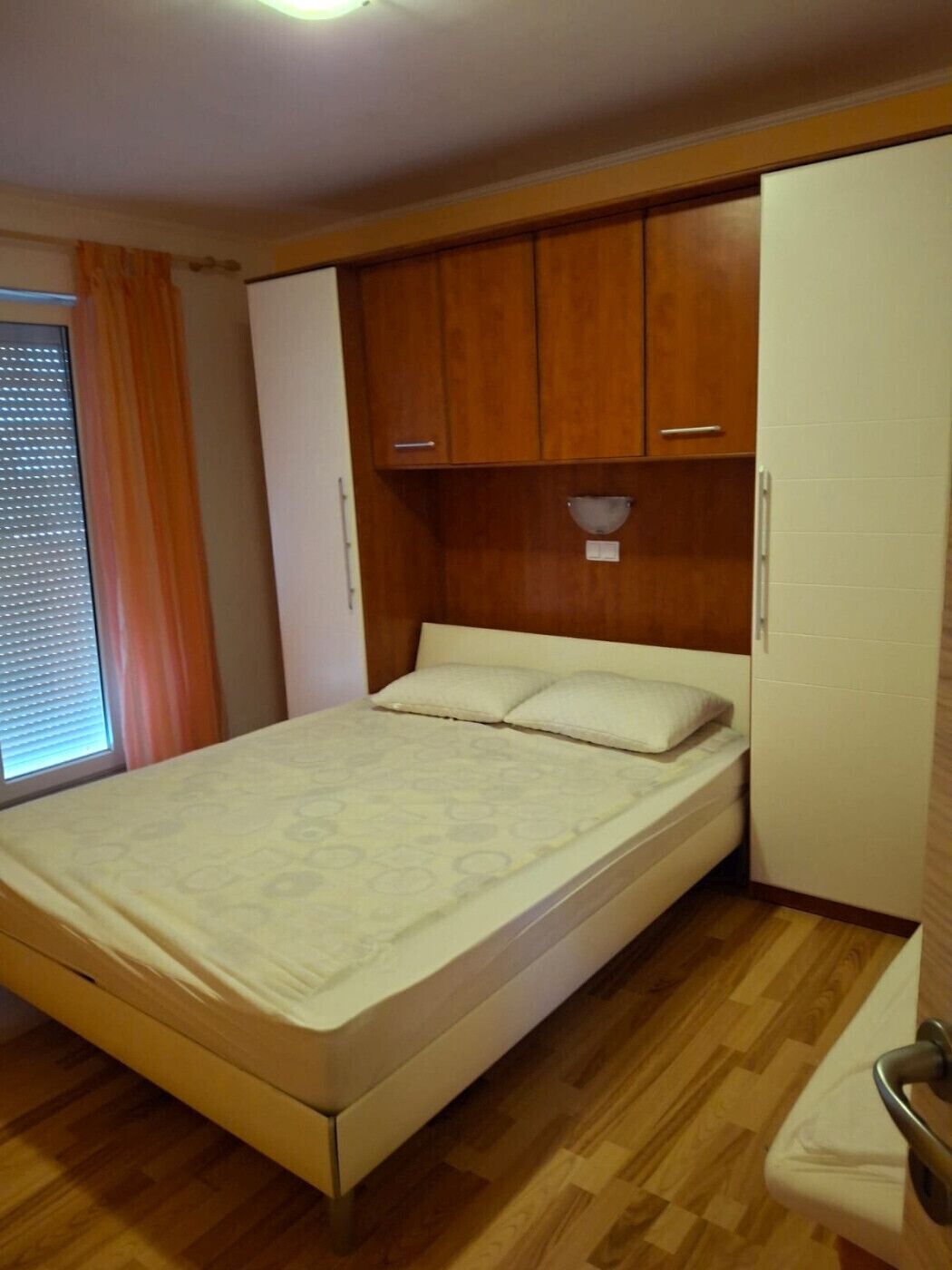 A bedroom with a bed, wooden wardrobe, and a small white cabinet.