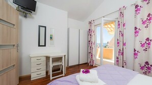 Ein Schlafzimmer mit Bett, Schreibtisch, Fernseher und einem Balkon mit Vorhängen.