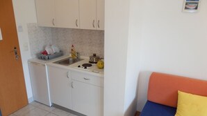 A compact kitchen with white cabinets, a built-in sink, and a stove. There is a small dining area with a blue sofa and a yellow pillow. - Studio apartment in Duće with Seaview, Balcony, Air condition, WIFI (4173-7) (Duce)
