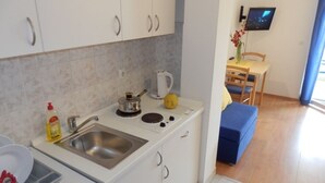 A compact kitchen with a sink, kettle, and a dining area with a blue sofa and a TV. - Studio apartment in Duće with Seaview, Balcony, Air condition, WIFI (4173-7) (Duce)