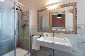Ein modernes Badezimmer mit einer Duschkabine aus Glas, einem weißen Waschbecken und einem Spiegel mit Mosaik-Rahmen.