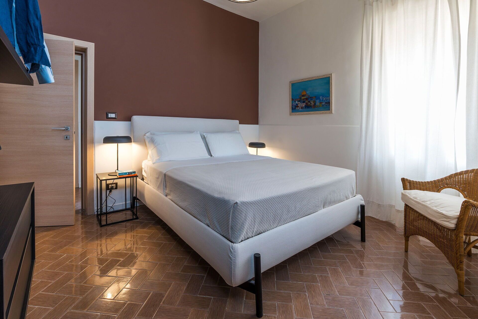A hotel room with a bed, bedside tables, a chair, and a painting on the wall.