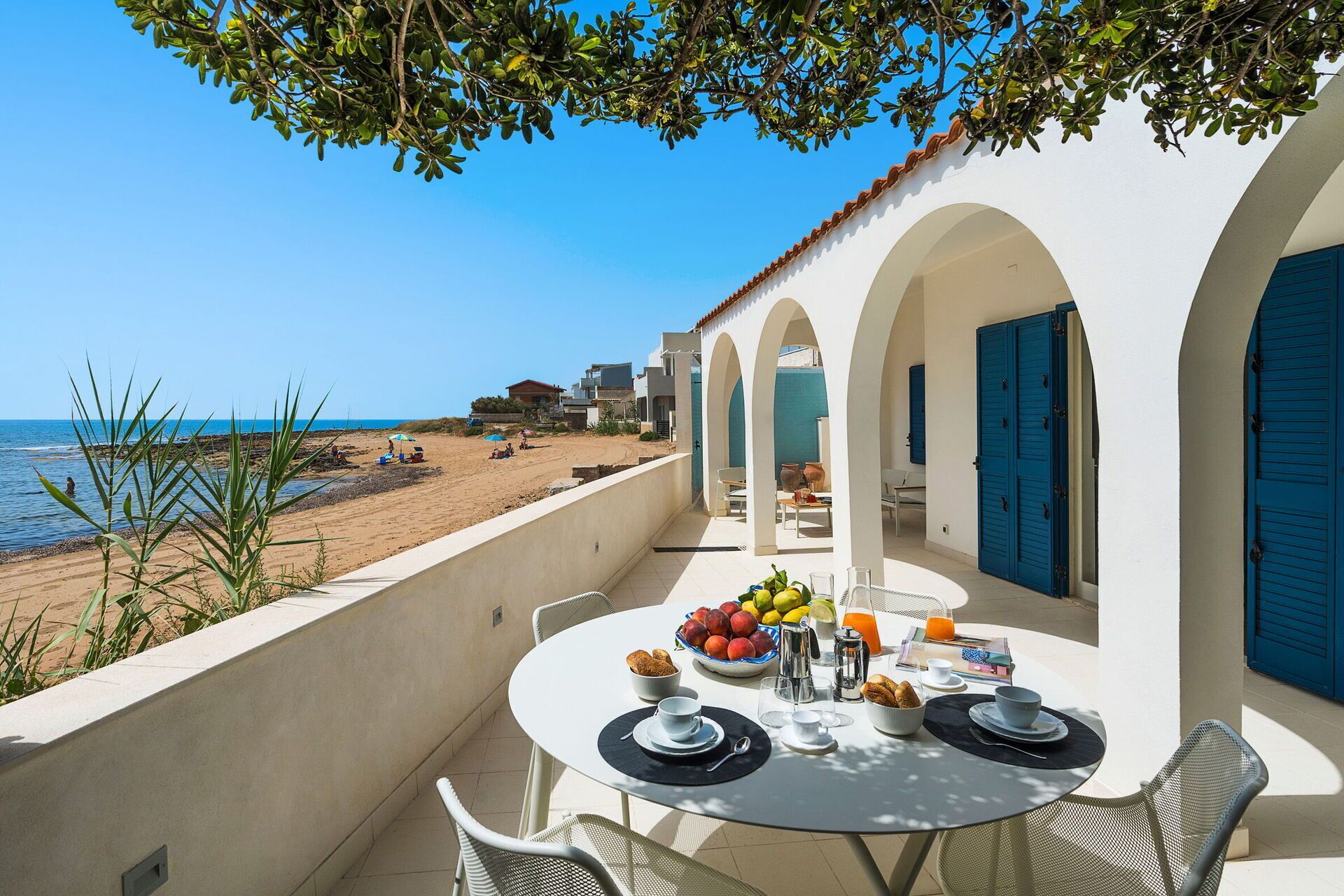 A terrace with a table set for breakfast overlooking a beach.