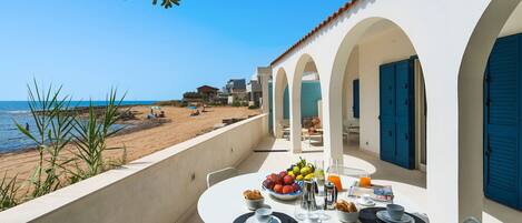 A terrace with a table set for breakfast overlooking a beach.