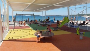Un espacio al aire libre techado con un parque infantil, que incluye columpios y toboganes, con vistas a un cuerpo de agua.