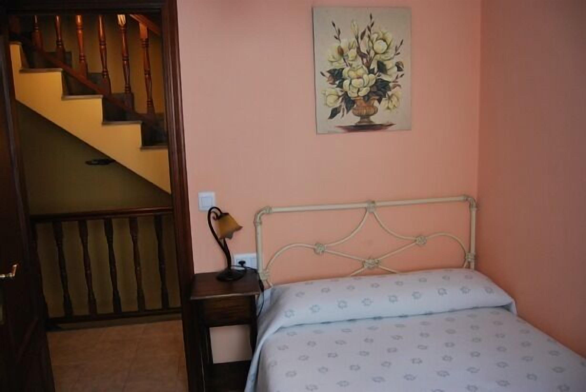 Une chambre à coucher avec un lit, une table de chevet, une lampe, un tableau au mur et un escalier menant à une autre pièce.