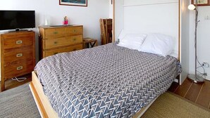 Un dormitorio con cama, cómoda de madera, televisión y una obra de arte en la pared.