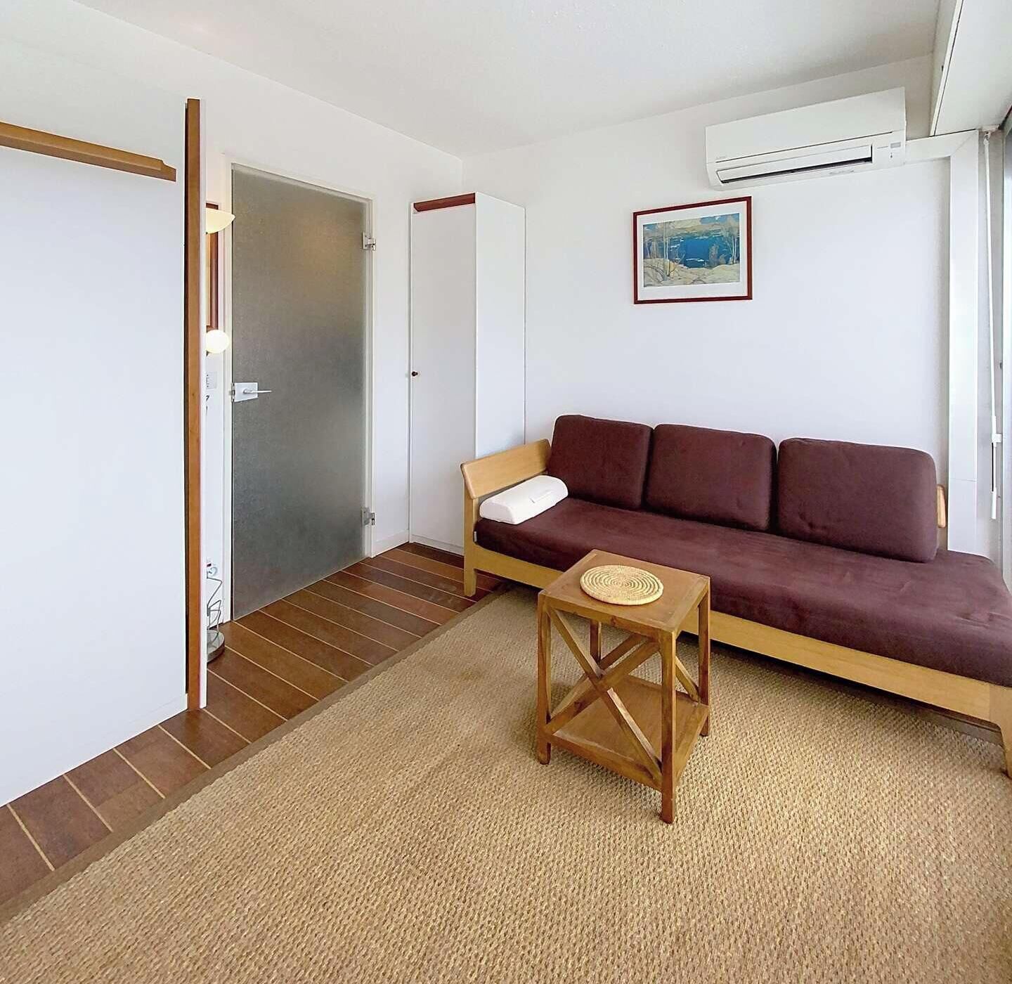 Une pièce avec un canapé marron, une petite table en bois et une porte qui donne sur une autre pièce.