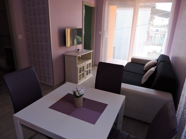 A living room with a white table, two chairs, a sofa, and a TV on a stand.