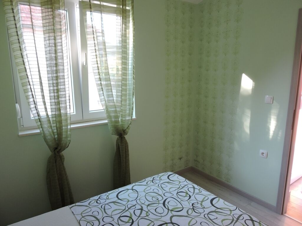 Una habitació amb un llit, dues finestres amb cortines transparents i una paret amb un disseny decoratiu.