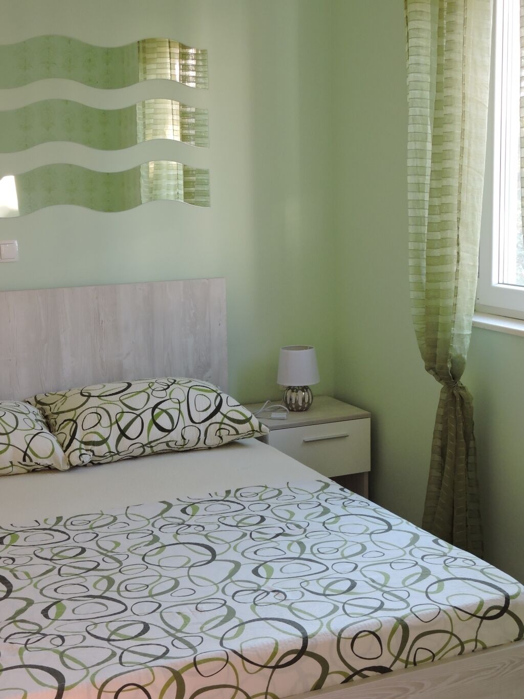 A bedroom with a bed, a nightstand, a lamp, and a window with curtains.
