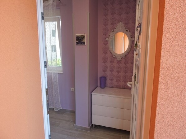 A narrow hallway with a door leading to a room with a vanity and a mirror.