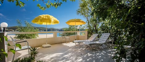 A rooftop terrace with two yellow umbrellas, lounge chairs, and potted plants.