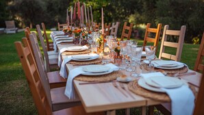 Una larga mesa de comedor al aire libre con sillas, platos, vasos y velas.