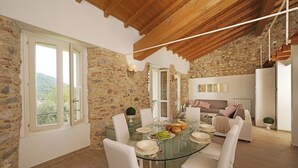 Comedor con mesa de vidrio, sillas blancas y paredes de piedra.