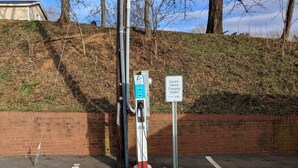 Una estación de carga para vehículos eléctricos con un muro de ladrillo y una colina cubierta de césped al fondo.