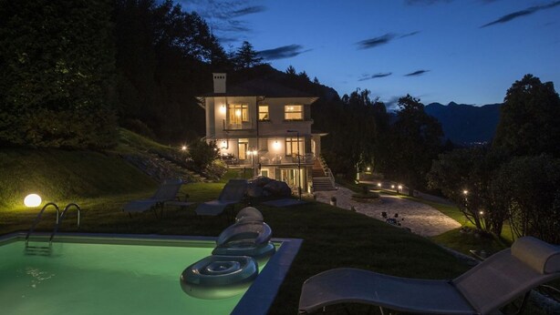 Ein zweistöckiges Haus mit Schwimmbad, Liegestühlen und einer Treppe zum Eingang.