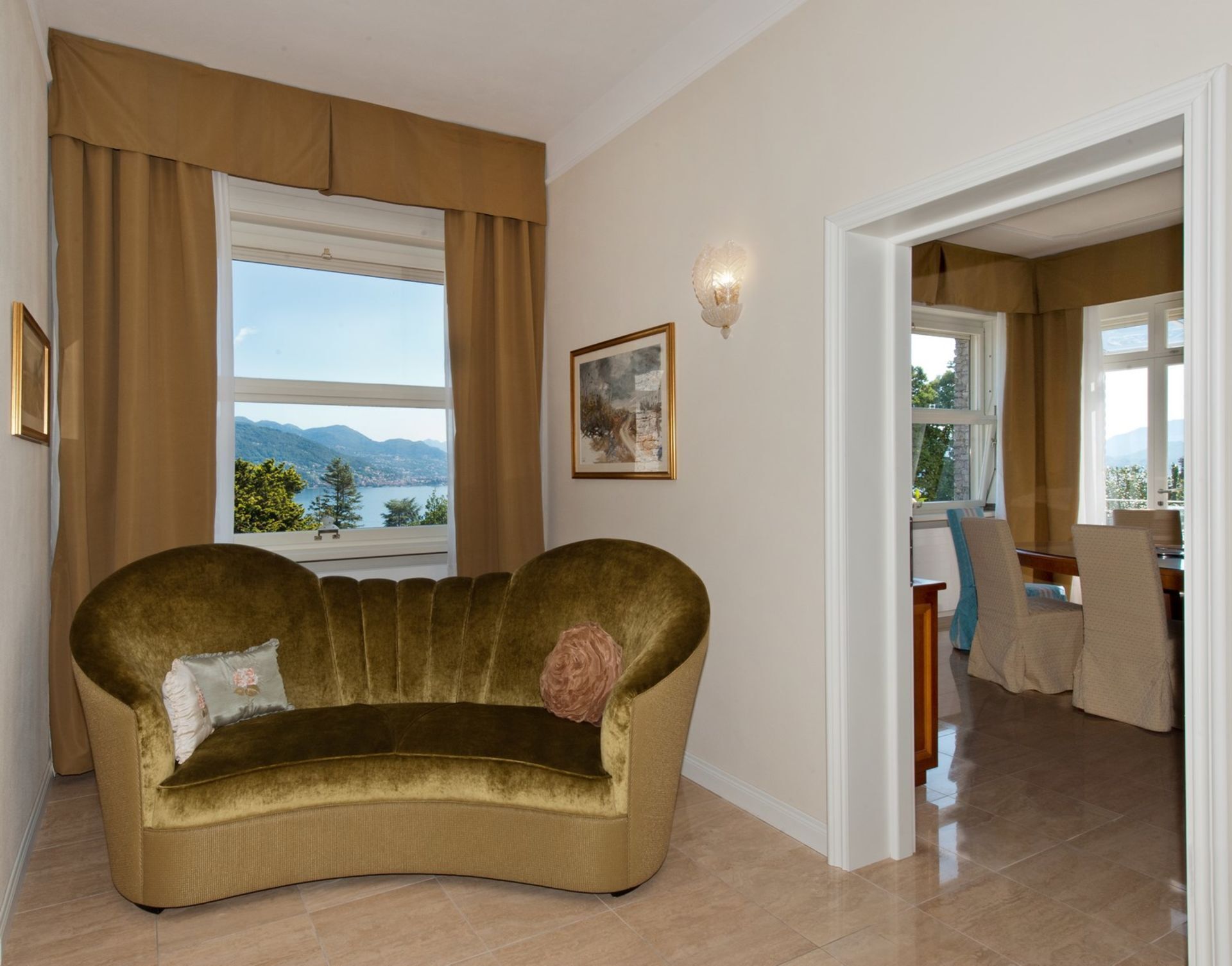 Un salón con sofá, un cuadro y vistas a montañas a través de una ventana.