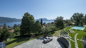 Ein Poolbereich mit einer Steinterrasse, einem Auto und Blick auf einen See und Berge.