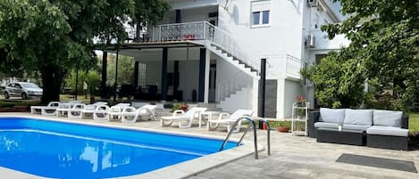 Een tweelaags huis met een zwembad, buitenmeubilair en een overdekt terras.