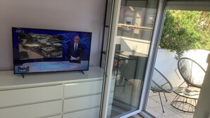 A television mounted on a white cabinet, a sliding glass door leading to an outdoor patio with chairs and a table, and a tiled floor. - Apartment in Bibinje with Terrace, Air condition, WIFI, Washing machine (877-2) (Bibinje)