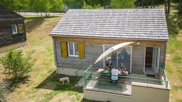 Een huis met twee verdiepingen met een balkon, een kleine hond op de grond en een persoon met een hond op het balkon.