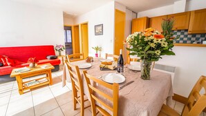 Een eetgedeelte met een tafel voor vier personen, houten stoelen, een rode bank, een klein bijzettafeltje en een vaas met bloemen.